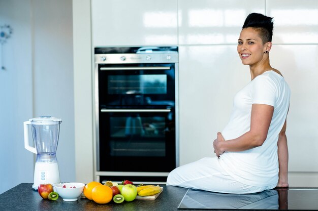 Mujer embarazada sentada en la encimera de la cocina y sonriendo