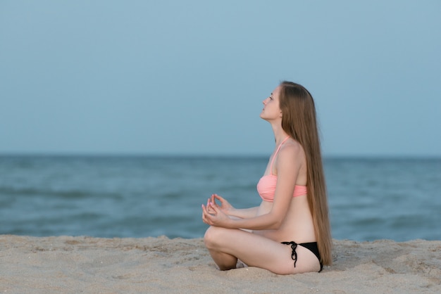 Mujer embarazada sentada en una playa y medita. Luz suave de la tarde, playa desierta.