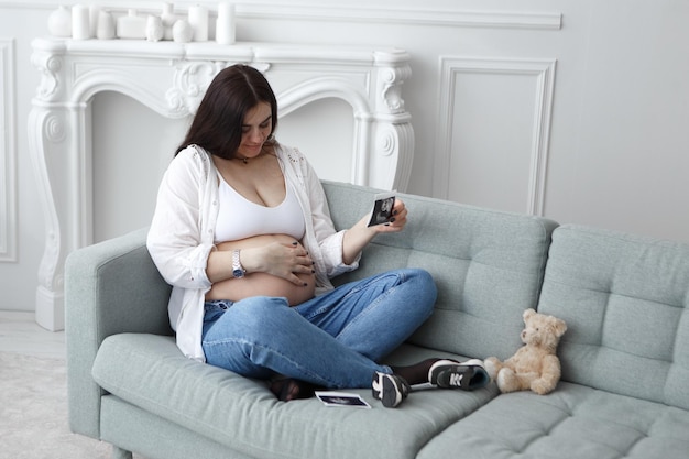 Mujer embarazada sentada sosteniendo la foto de ultrasonido de los golpes de vientre abdomen feto abdomen