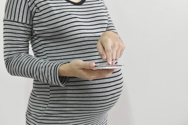 Mujer embarazada con smartphone en espacio de copia de fondo gris