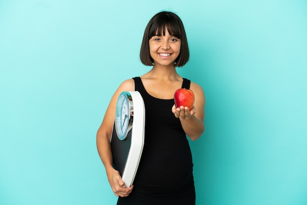 Mujer embarazada sobre fondo aislado sosteniendo una balanza y ofreciendo una manzana