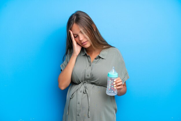 Mujer embarazada sobre fondo azul con dolor de cabeza