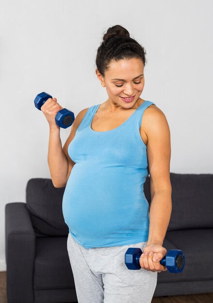 Mujer embarazada sonriente en casa entrenando con pesas