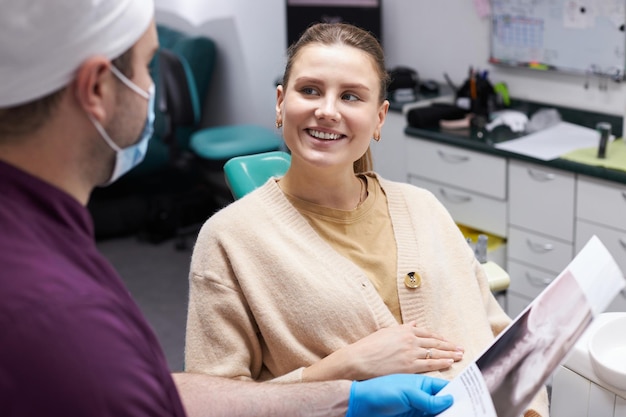 Mujer embarazada sonriente mirando al dentista explicando la película dental Xray en la clínica de odontología