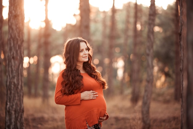 Una mujer embarazada sonriente usa ropa informal posando en el parque al aire libre