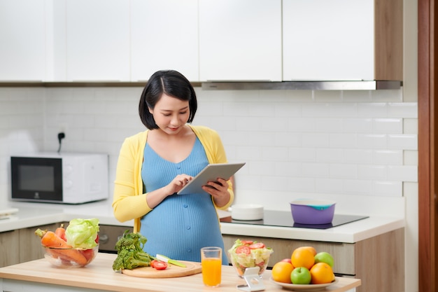 Mujer embarazada sosteniendo la almohadilla de la tableta mirando la lista y comprobando verduras frescas.