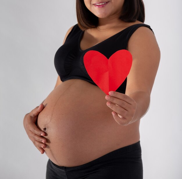 Mujer embarazada sosteniendo un corazón de papel rojo