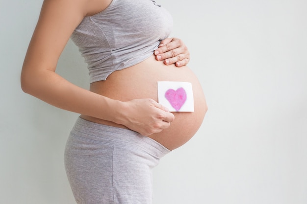 Mujer embarazada sosteniendo corazón rojo y mano sobre su vientre, símbolo de nueva vida