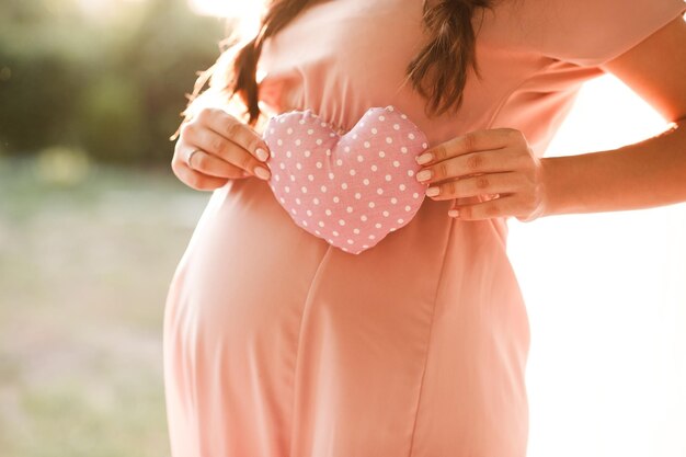 Mujer embarazada sosteniendo un corazón rosa al aire libre maternidad maternidad