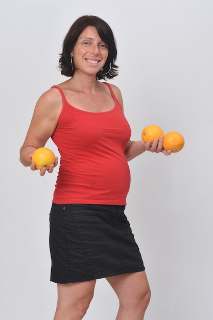 Mujer embarazada sosteniendo una fruta naranja sobre fondo blanco.