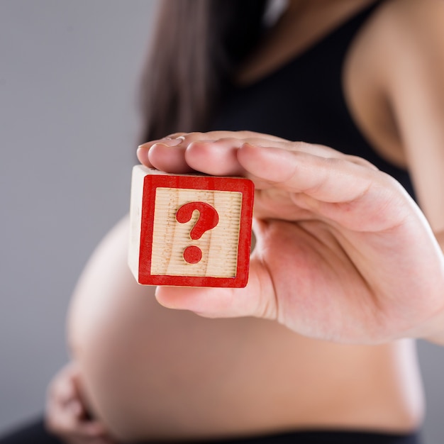 Mujer embarazada sosteniendo madera de cubo con signo de interrogación para bebé. Hijos o niñas.