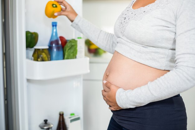 Mujer embarazada sosteniendo el pimiento del refrigerador