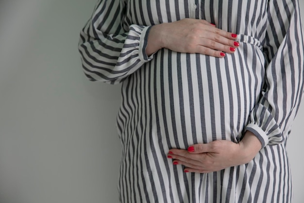 Una mujer embarazada sosteniendo su barriga de bebé se paró contra un fondo liso