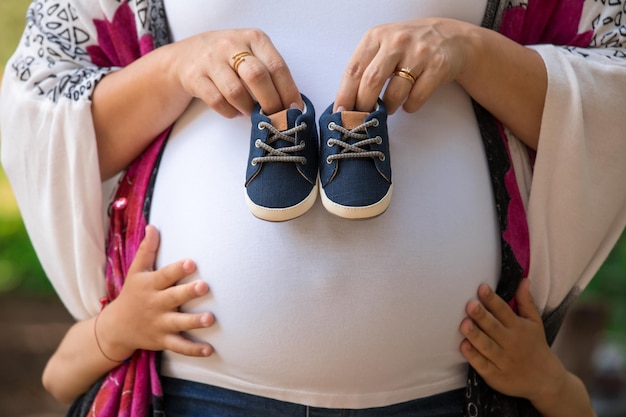 Una mujer embarazada sostiene un par de zapatos de bebé.