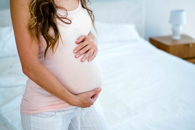 Foto mujer embarazada, en su habitación, sosteniendo su bulto