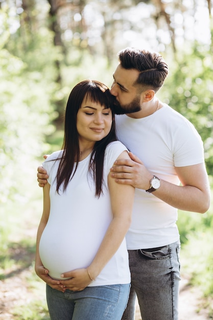 Mujer embarazada y su marido beaeded abrazando en la barriga juntos en la naturaleza al aire libre