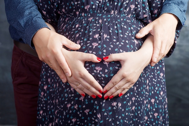 Mujer embarazada y su marido sosteniendo haciendo forma de corazón con las manos en el vientre embarazado