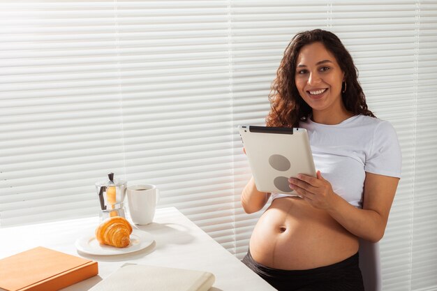 Mujer embarazada con tableta digital. hora del desayuno. concepto de tecnología y embarazo.