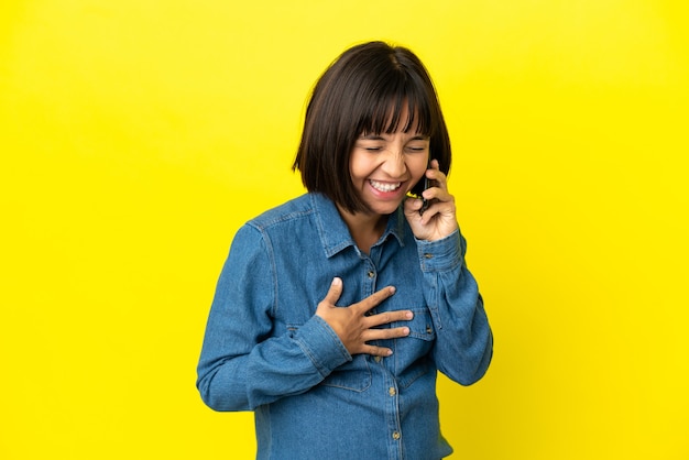 Mujer embarazada con teléfono móvil aislado sobre fondo amarillo sonriendo mucho