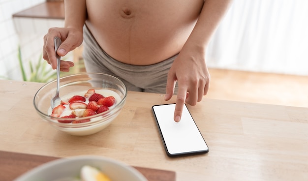 Foto mujer embarazada con teléfono móvil mientras tiene alimentos saludables.