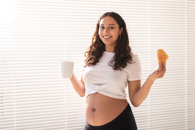 Mujer embarazada, tenencia, croissant, y, taza de café