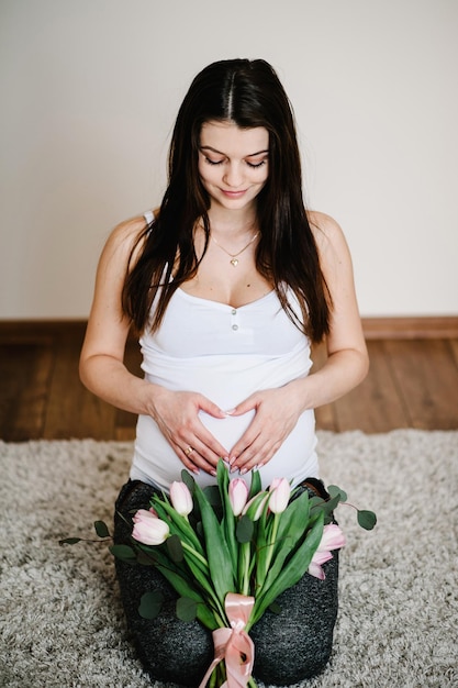 mujer embarazada, tenencia, vientre, con, un, ramo de flores, abrazar, panza, elaboración, símbolo, corazón, manos, en casa, baby shower, maternidad, concepto, niña, en, foto