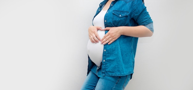 La mujer embarazada tiene las manos sobre el vientre sobre un fondo gris. Concepto de embarazo, maternidad, preparación y expectativa.