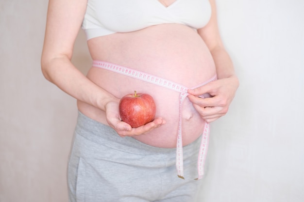 Una mujer embarazada tiene una manzana roja en la mano. El concepto de nutrición adecuada
