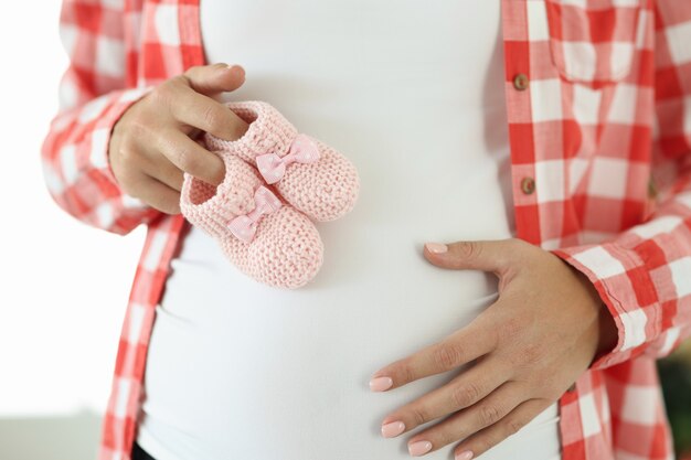 La mujer embarazada tiene zapatillas rosas para recién nacido. Concepto de embarazo