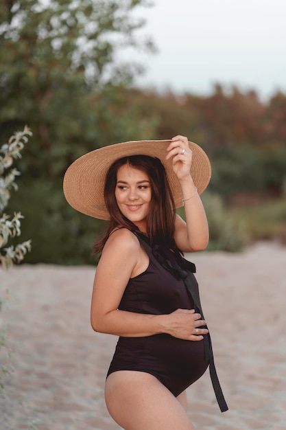 mujer embarazada en traje de baño negro y sombrero en una playa de arena