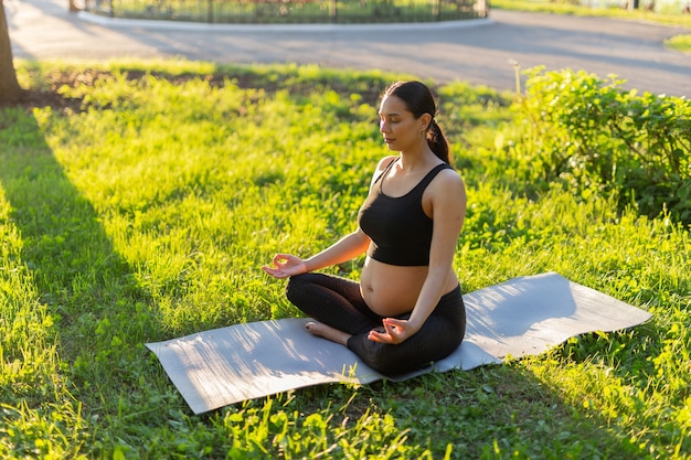 Mujer embarazada en traje de gimnasia hace yoga y medita sentado en la estera