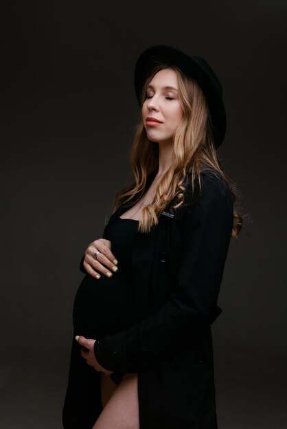 Una mujer embarazada con un traje negro y un sombrero negro. Espacio para copiar. El concepto de digestión saludable, estilo de vida, FIV