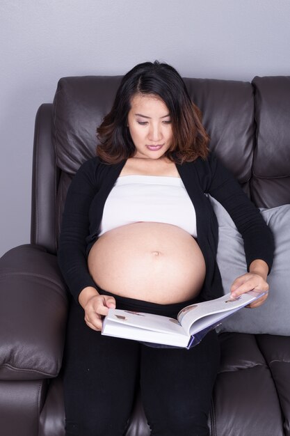 mujer embarazada tumbada en el sofá y leyendo el libro