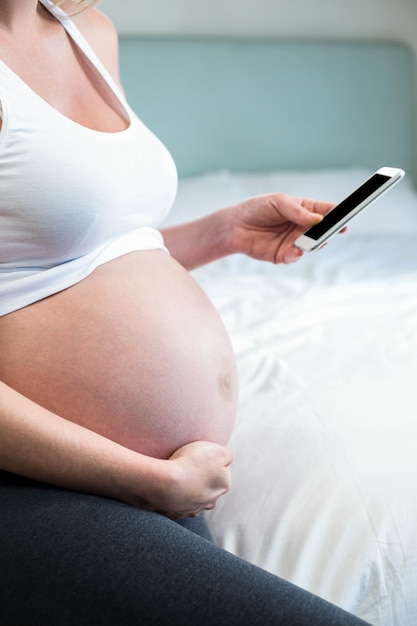 Mujer embarazada usando teléfono inteligente en su cama