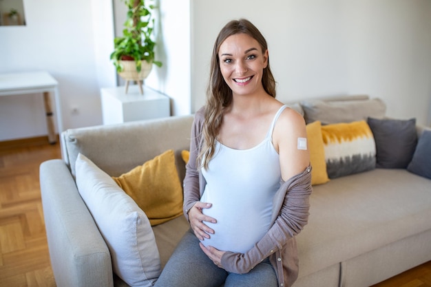 Mujer embarazada vacunada contra Covid19 mostrando el brazo con vendaje de yeso después de la inyección de la vacuna contra el coronavirus sentada sonriendo a la cámara