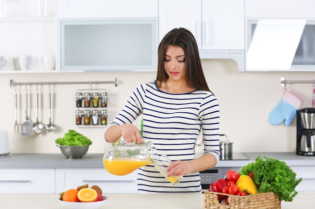 Mujer embarazada vertiendo jugo de naranja en un vaso en la cocina