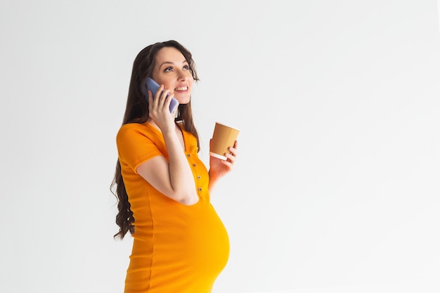 mujer embarazada, en, vestido amarillo, hablar teléfono, mujer embarazada joven, blanco, plano de fondo