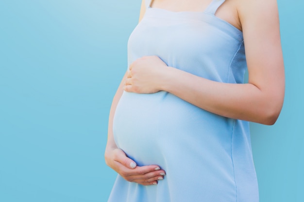 Una mujer embarazada en un vestido azul en azul. Concepto de embarazo