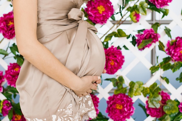 Una mujer embarazada con un vestido beige sostiene sus manos sobre su estómago Maternidad Esperando un hijo