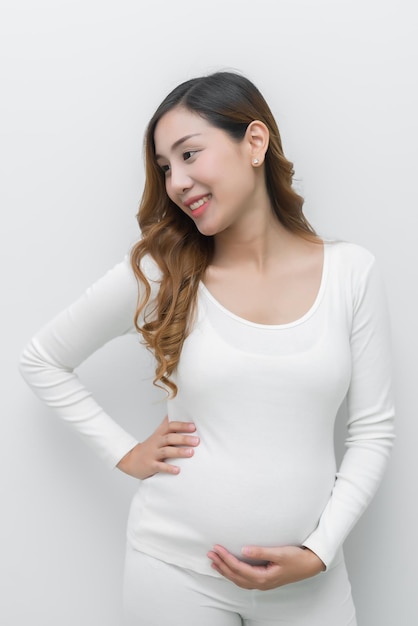 Una mujer embarazada con vestido blanco de pie sosteniendo su vientre