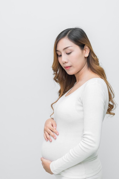 Una mujer embarazada con vestido blanco posa para tomar una foto con fondo blanco