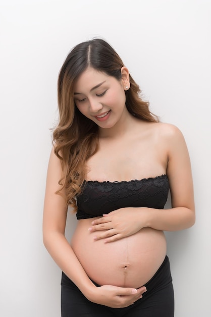 Mujer embarazada con vestido blanco toca su vientre sobre fondo blanco mujer asiática