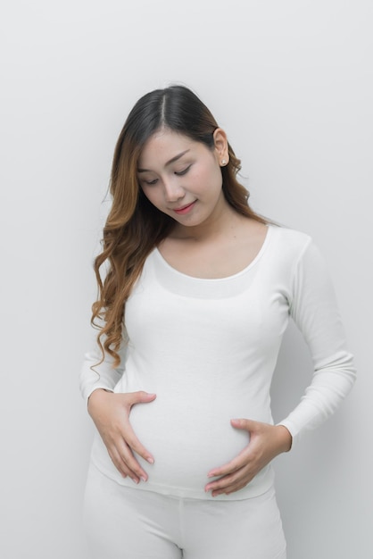 Mujer embarazada en vestido blanco usa toque de mano en su vientre sobre fondo blanco mujer asiática gente de Tailandia