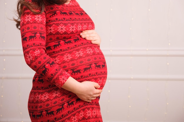 Una mujer embarazada con un vestido rojo se acaricia el vientre.