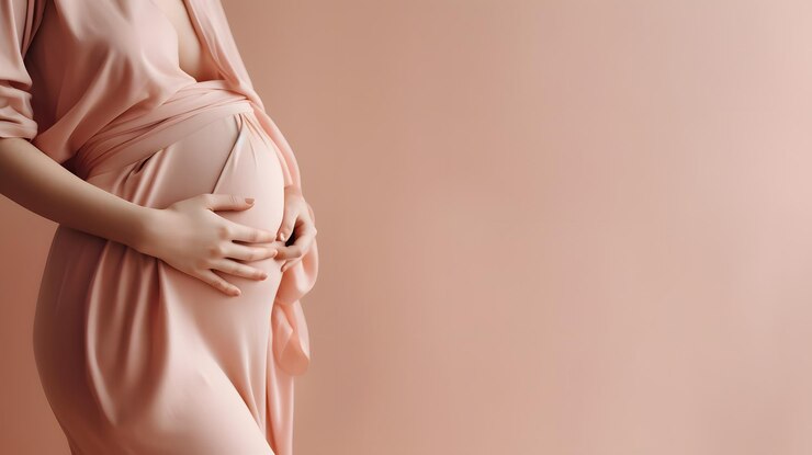 Una mujer embarazada con un vestido rosa sostiene su vientre.