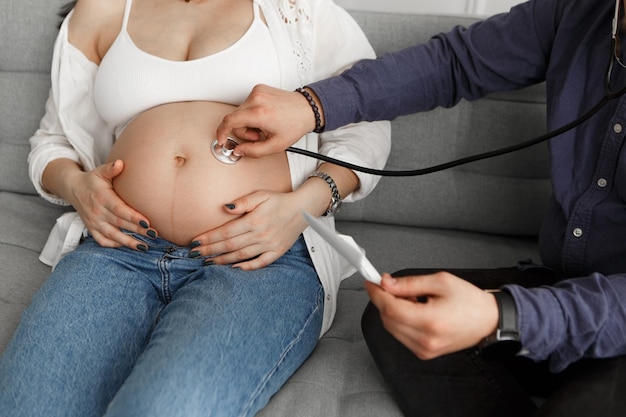 Mujer embarazada visitando al médico sostiene la foto de ultrasonido escucha el vientre con el estetoscopio
