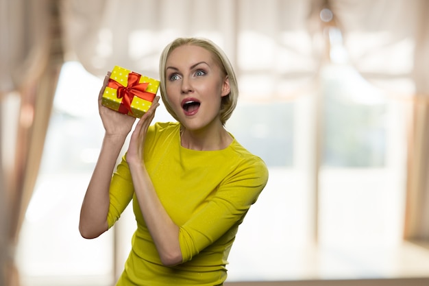 Mujer emocionada con la boca abierta sosteniendo una pequeña caja de regalo