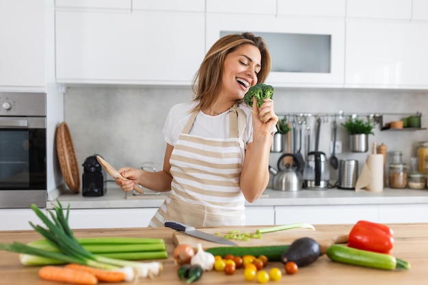 Mujer emocionada cantando y bailando en una cocina moderna en casa mujer feliz sosteniendo una espátula como micrófono bailando escuchando música divirtiéndose con utensilios de cocina preparando el desayuno