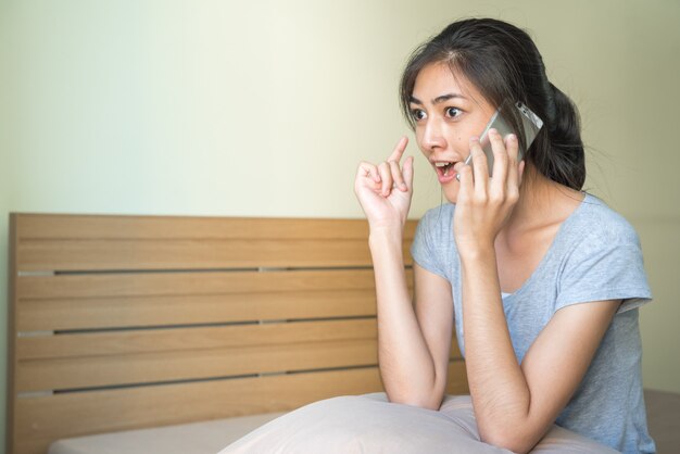 Mujer emocionada feliz que habla en el teléfono móvil en la cama.