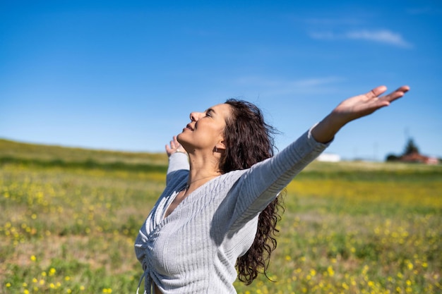 Mujer emocionada levantando los brazos y respirando aire fresco con fondo de cielo azul celebrando la primavera